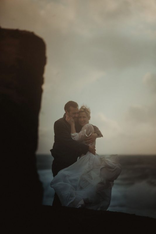 Dramatic Iceland wedding portrait of a couple posing in cold weather by the cliffs