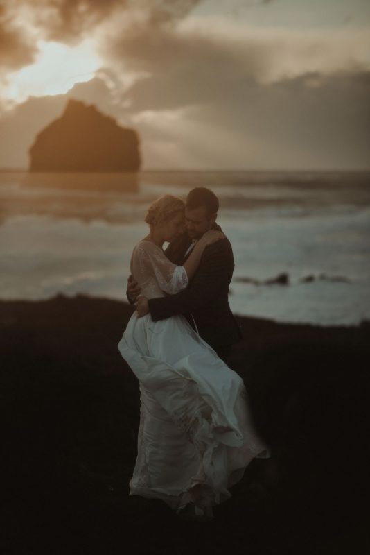 Dramatic Iceland wedding portrait of a couple posing in cold weather at sunset by the cliffs